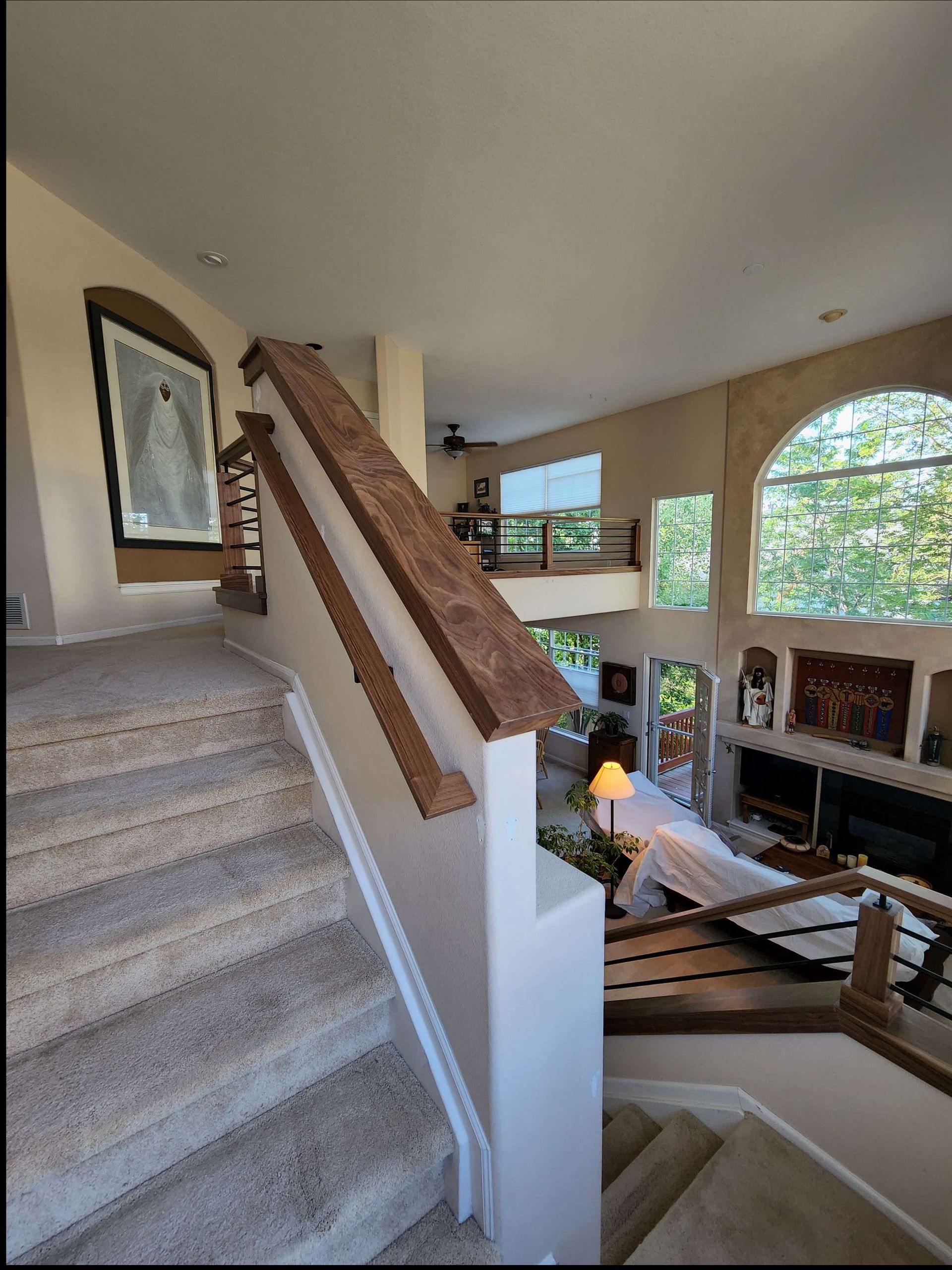 Staircase with wooden railing, leading to a living area with natural light and an arched window.