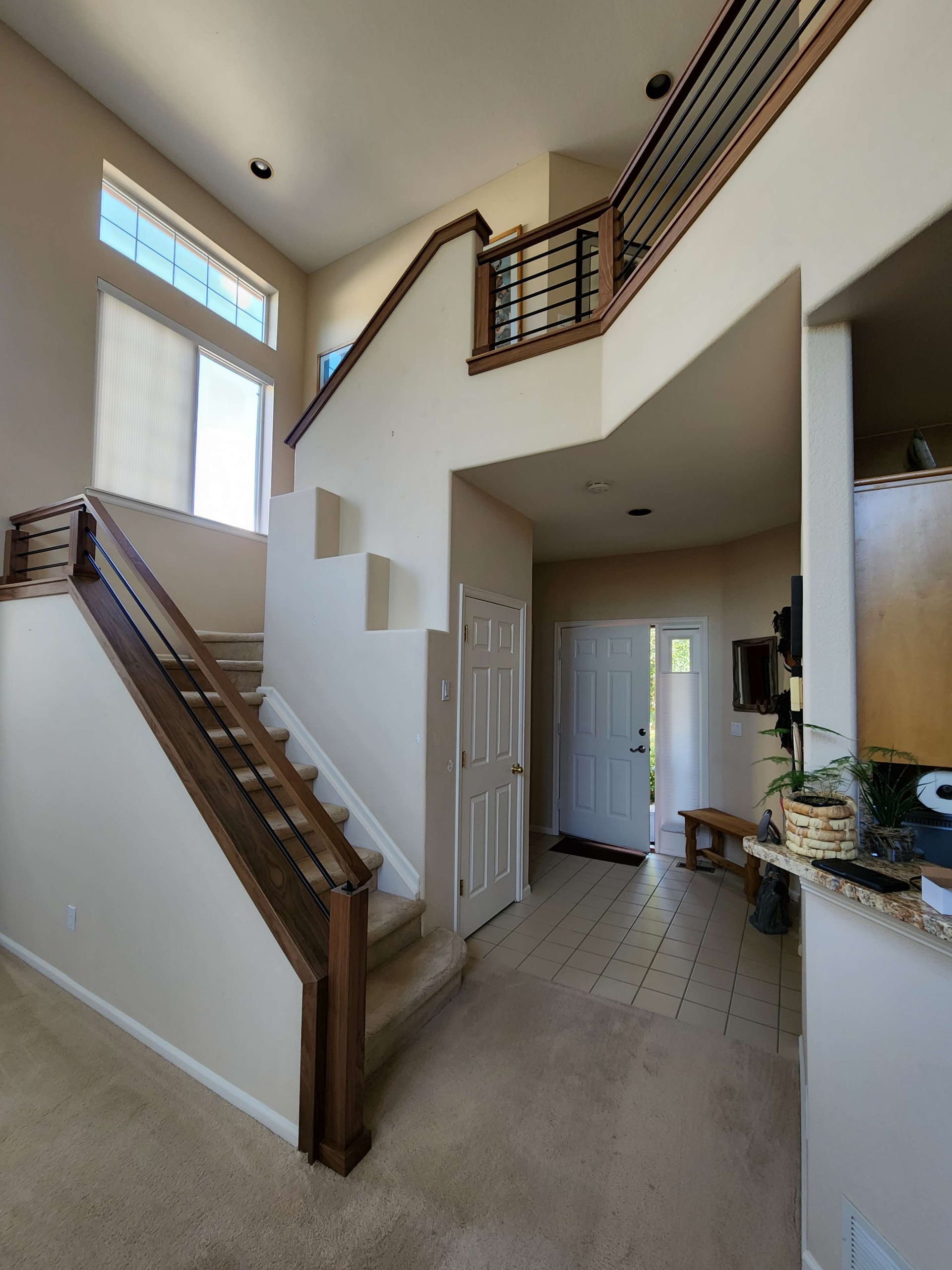 A two-story entryway with a staircase, a door, and natural light from tall windows.