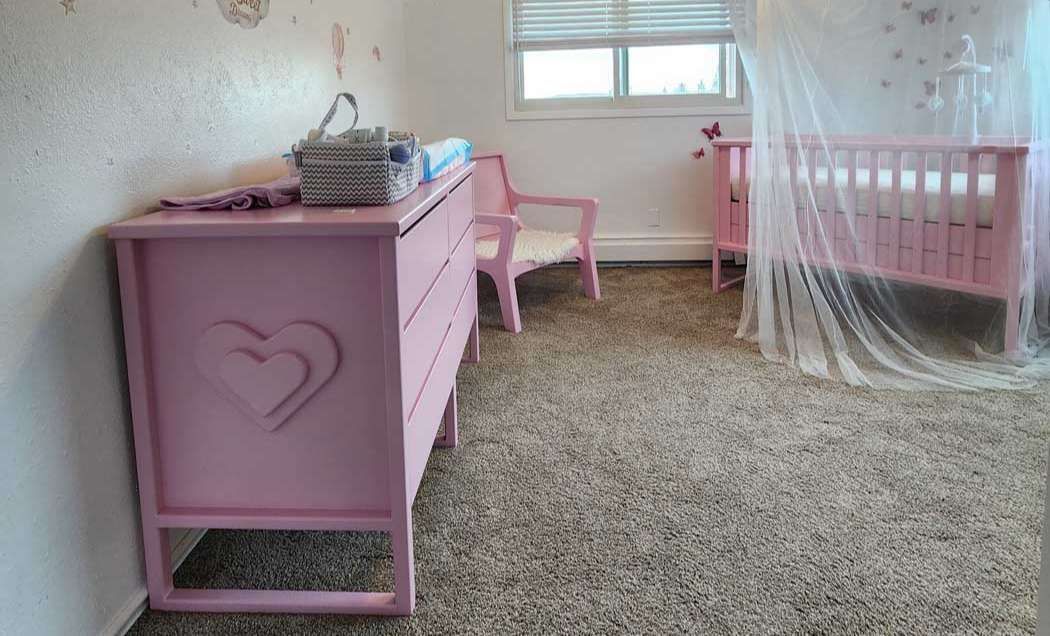 Pink nursery room with dresser, crib, chair, and fluffy rug.