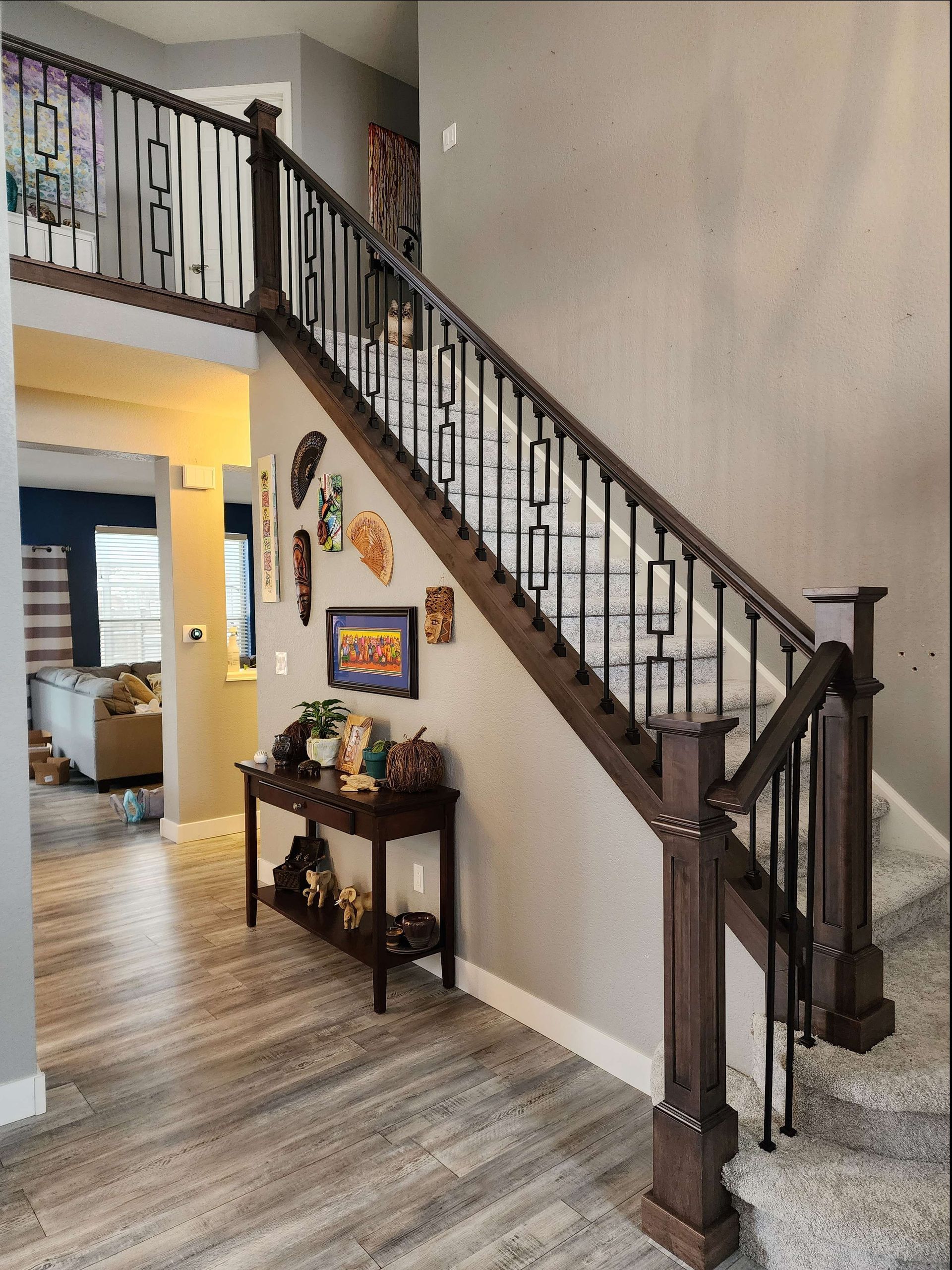 Staircase with dark wood railing, black iron balusters, and gray walls.  A console table and artwork are visible.