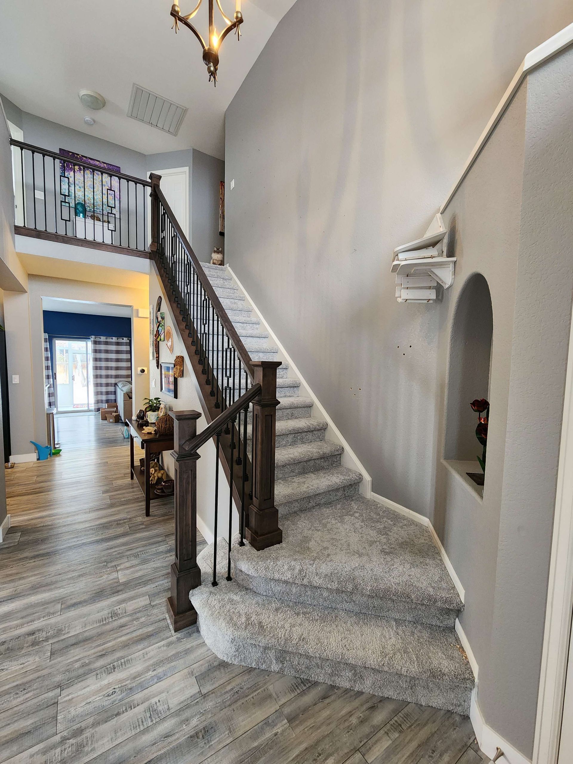 Staircase with gray carpet, brown railing, and gray walls leads to a second floor overlooking a hallway.