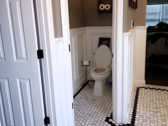 Bathroom with white toilet, white wainscoting, and black and white patterned tile floor.