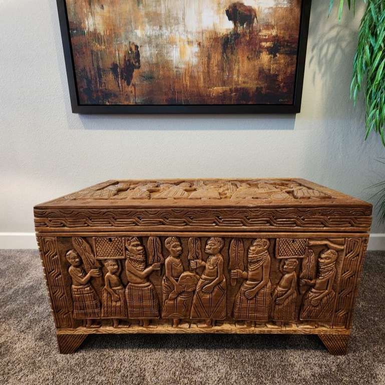 Ornate wooden chest with carved figures, beneath a framed landscape painting.