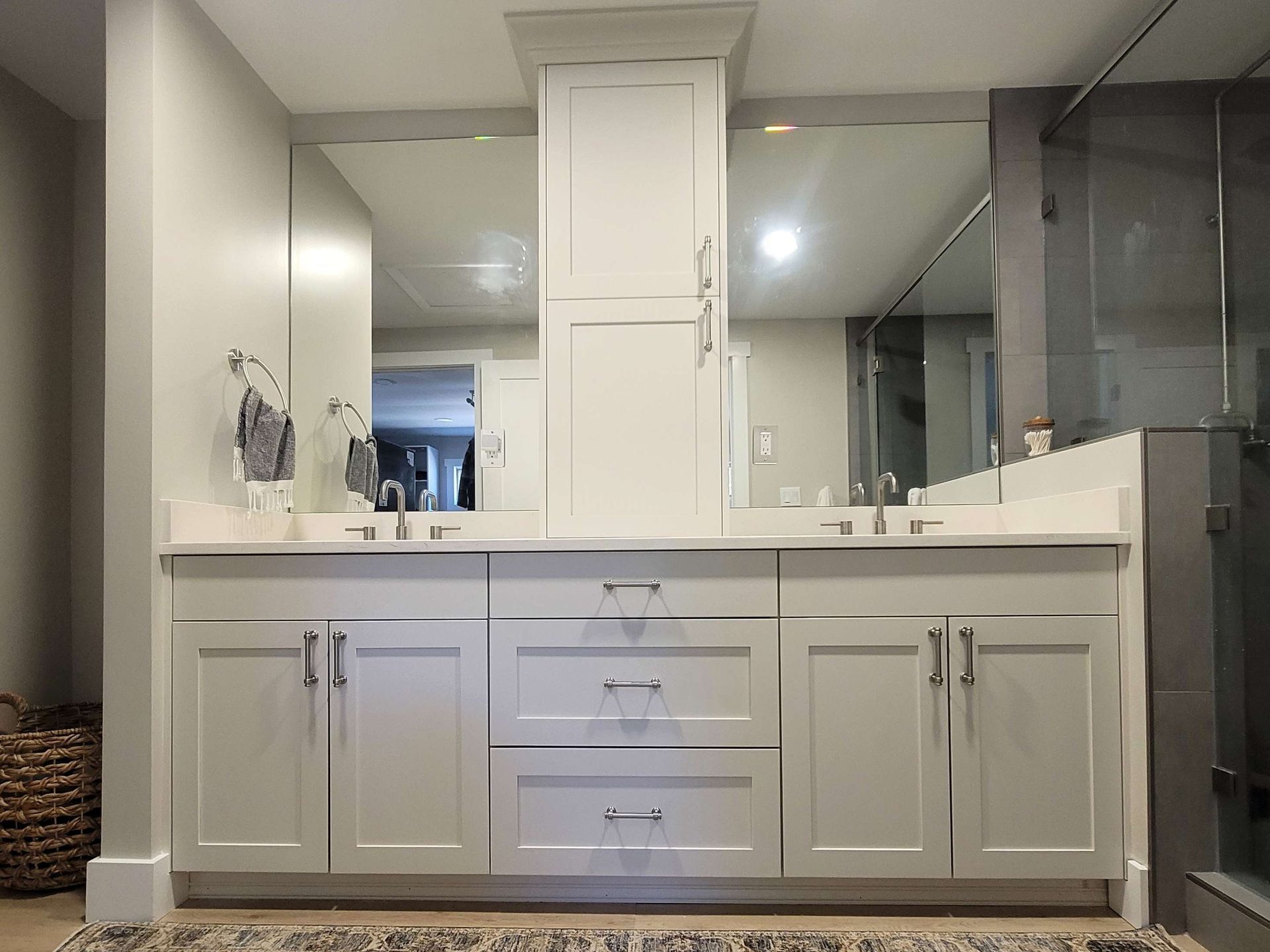 Bathroom vanity with white cabinets, countertop, mirrors, and a tall central cabinet.