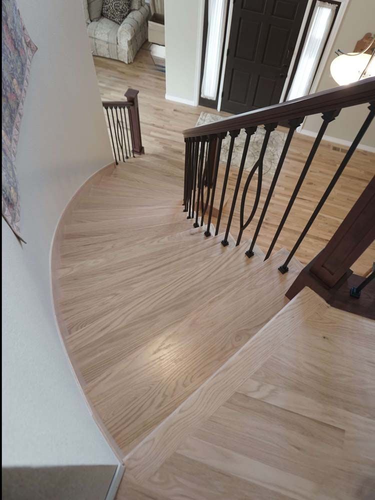 Wooden staircase with a curved landing, black iron railing, and a dark front door.