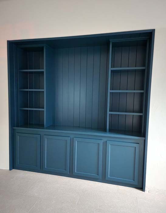 Built-in blue storage cabinet with shelves and closed door compartments, recessed in a white wall.