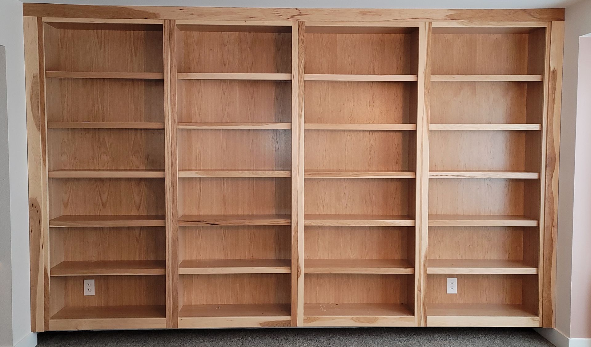 Wooden built-in bookshelves with four vertical sections, light wood, multiple shelves, electrical outlets visible.