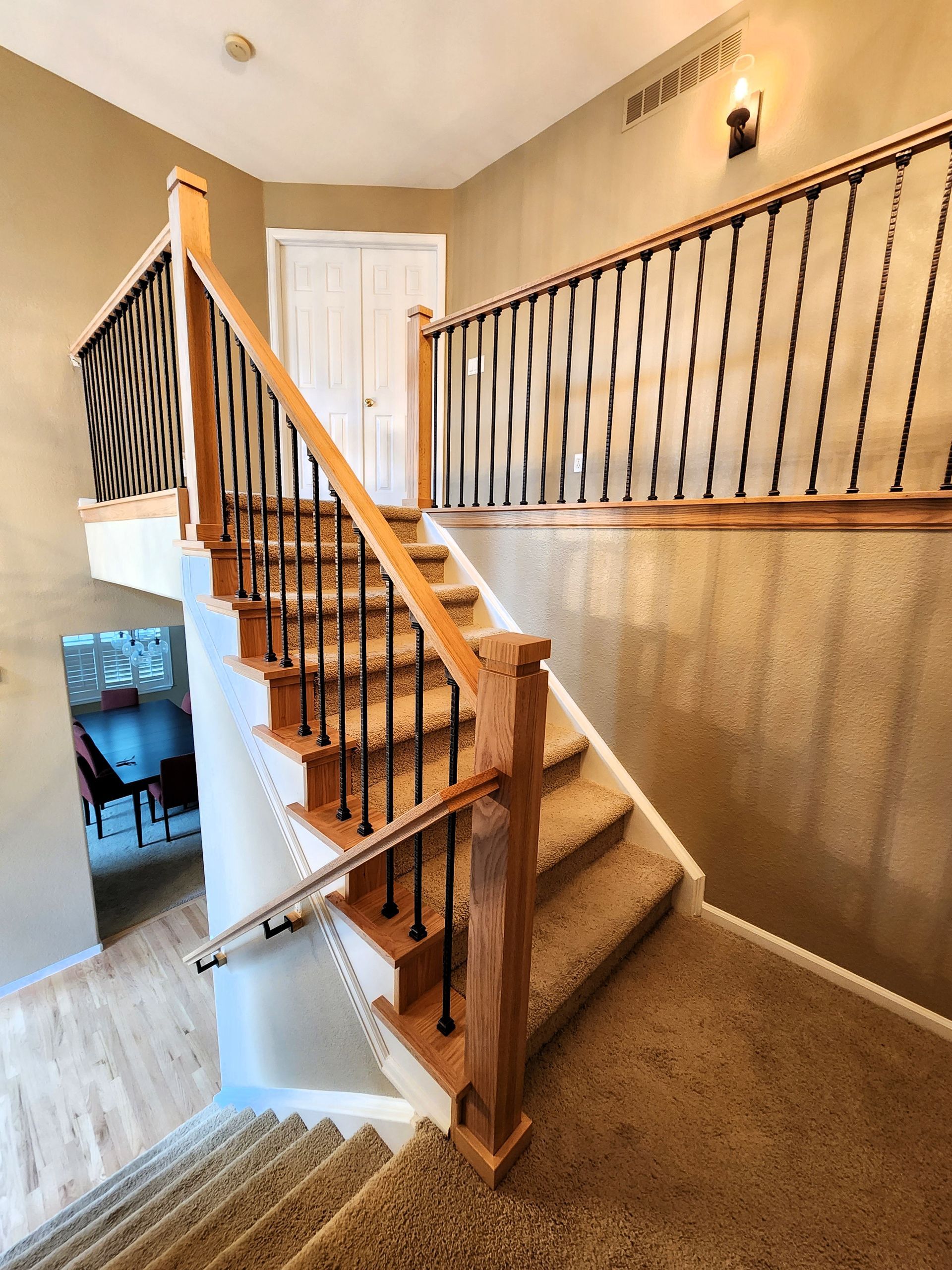 Wooden staircase with black iron spindles and beige carpet. Door at top of stairs.