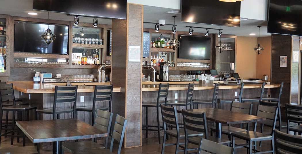 Interior of a bar and restaurant with tables, chairs, and a bar area with multiple TVs.