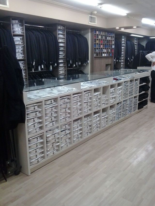 A clothing store displays rows of suits and drawers of accessories, with a light wooden floor.