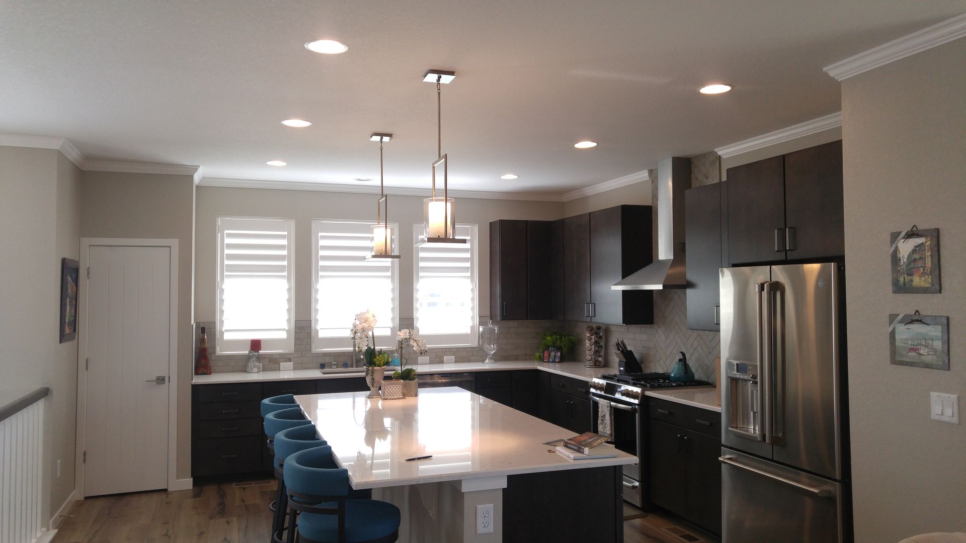 Modern kitchen with dark cabinets, white countertop island, stainless steel appliances, and pendant lights.