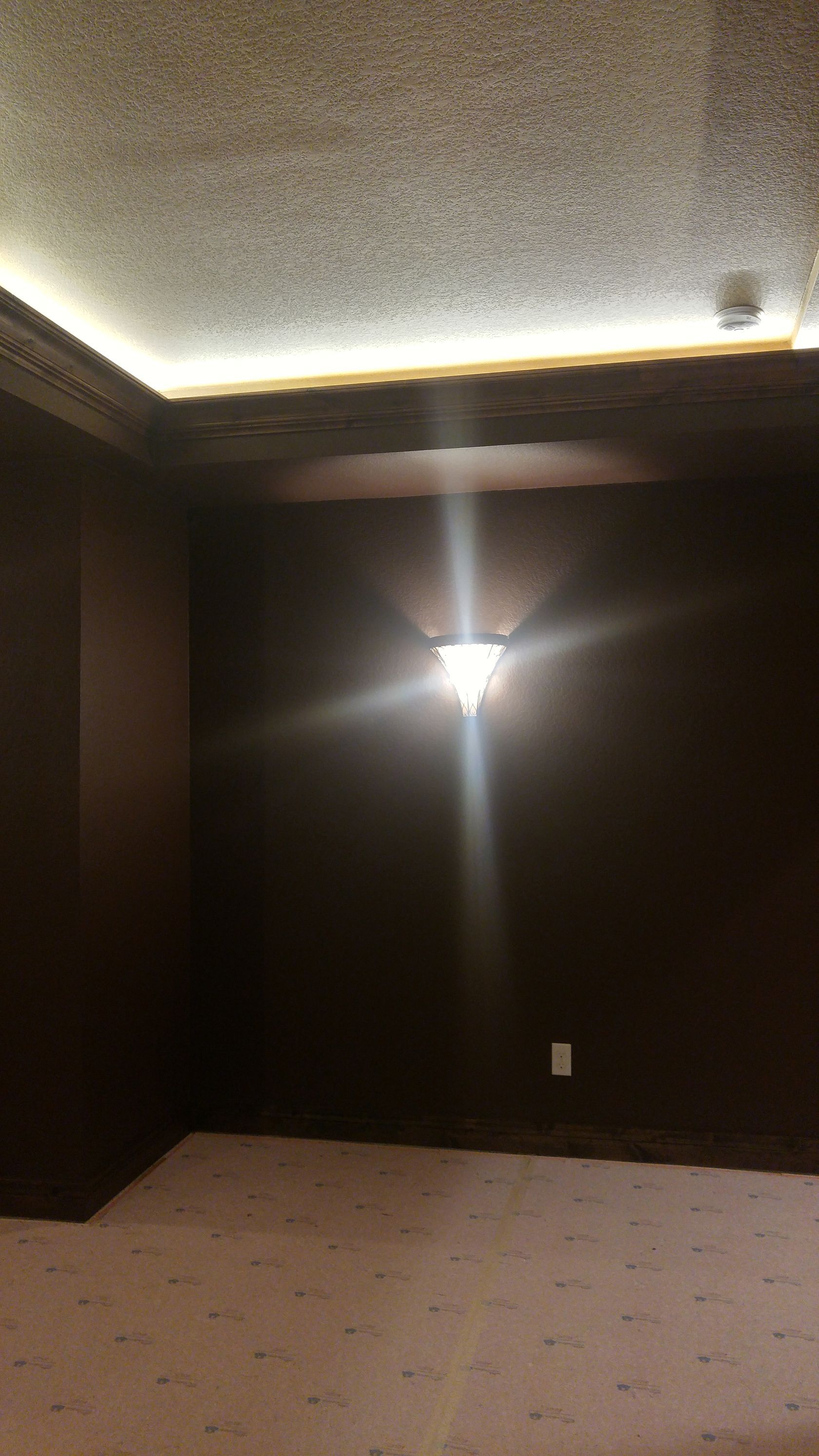 Dark brown room with a light fixture on the wall and a lighted ceiling trim.