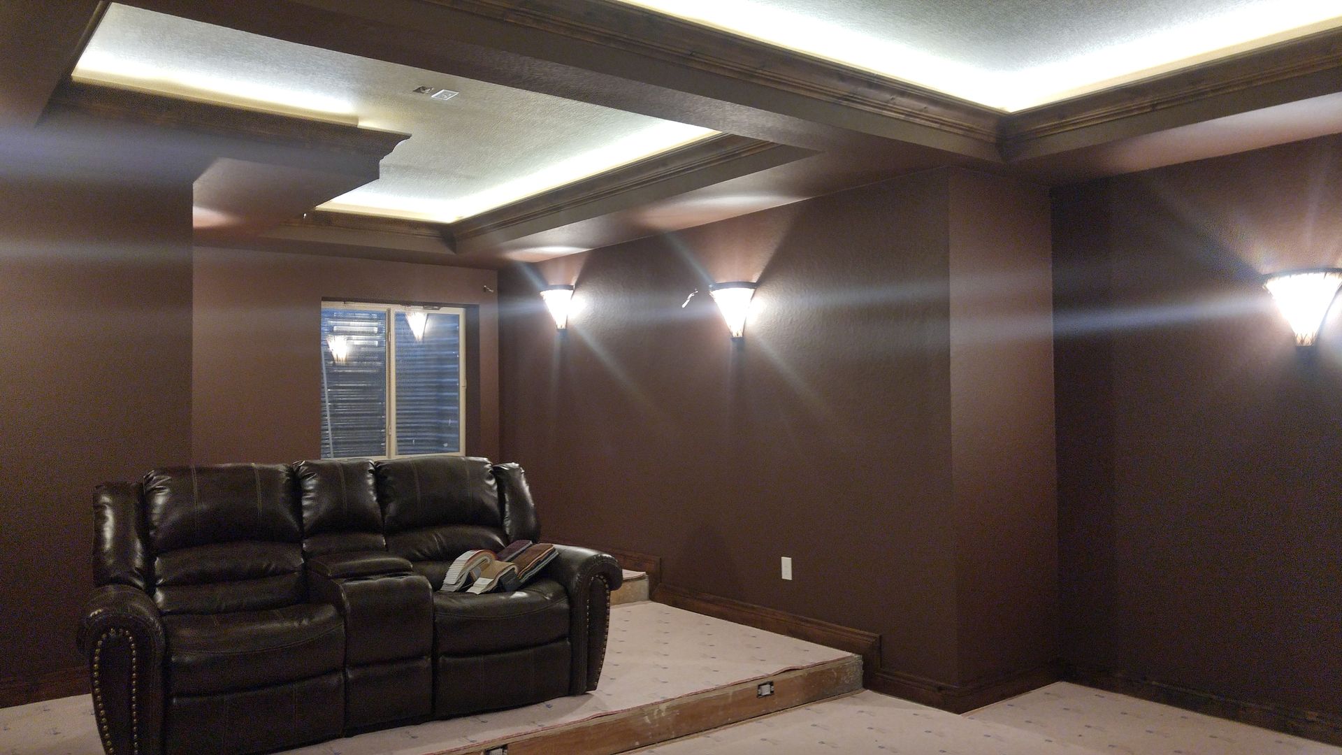 Brown home theater room with recessed lighting, brown walls, and leather couch on a raised platform.