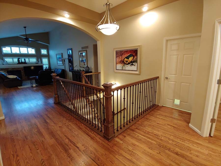 Wooden staircase with a dark banister, leading to a living room with a fireplace and windows.