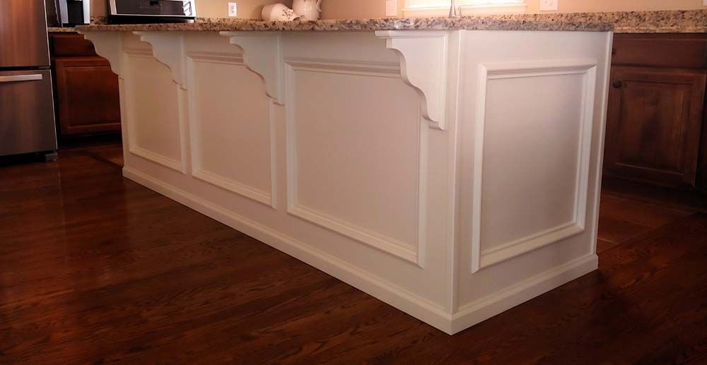 White kitchen island with granite countertop and dark wood floor.