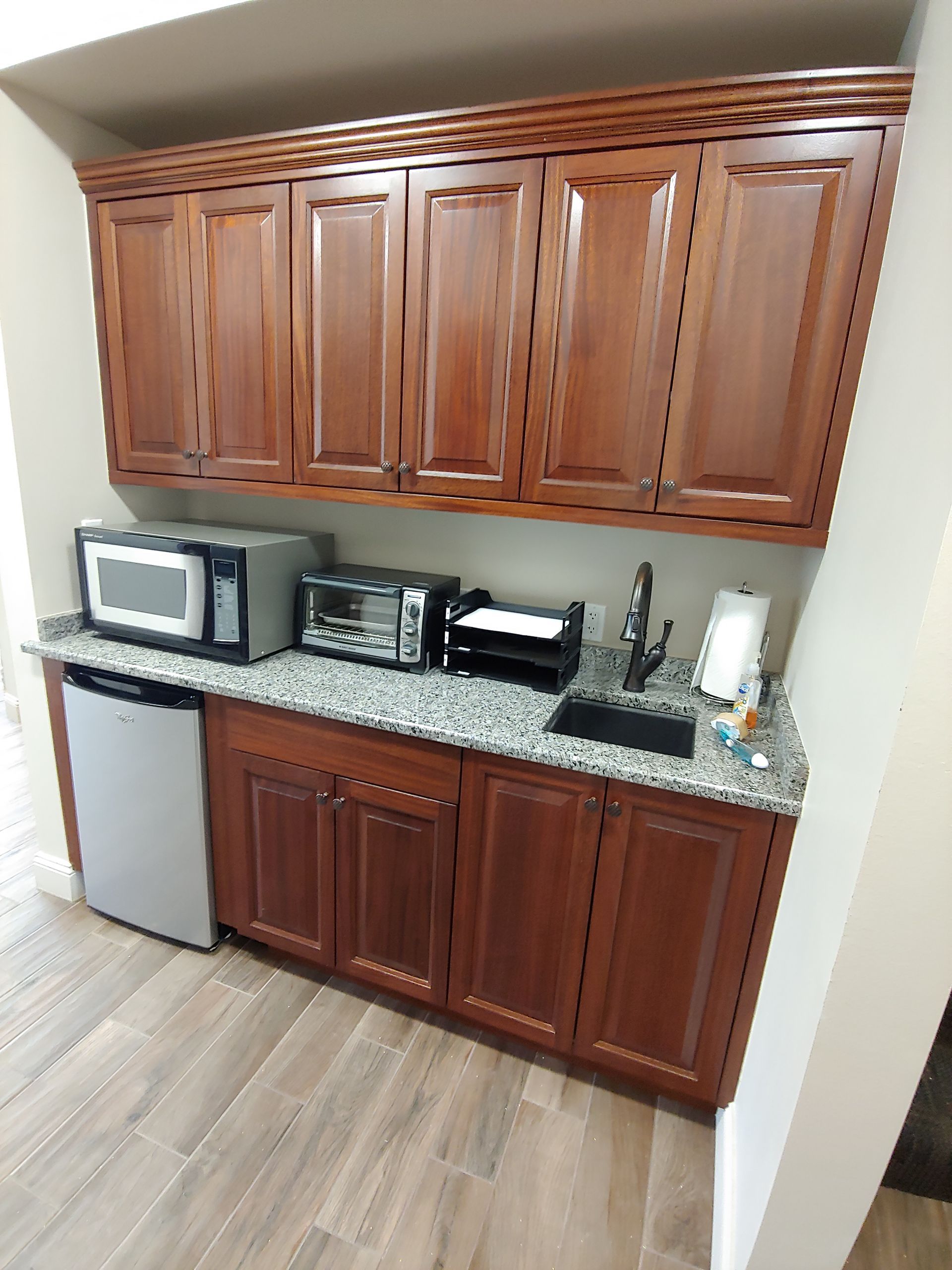Built-in kitchenette with brown cabinets, granite countertop, appliances, and small sink.