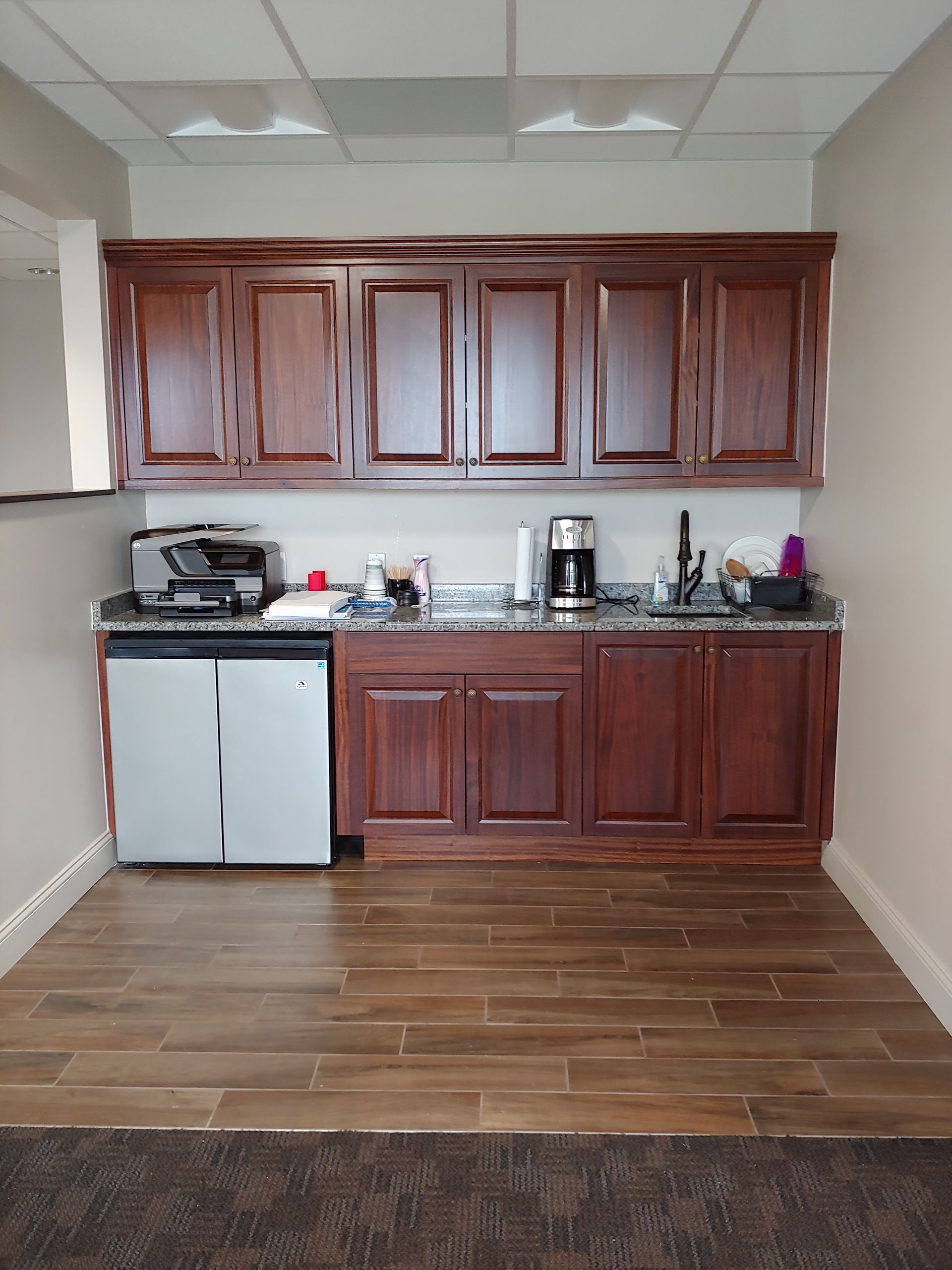 Office kitchenette with dark wood cabinets, a countertop, and a mini-refrigerator.