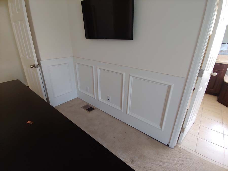 White paneled wall with a mounted TV above, next to a doorway and desk.