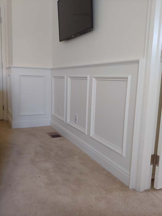 White paneled wall with a mounted television above. Beige carpeted floor.