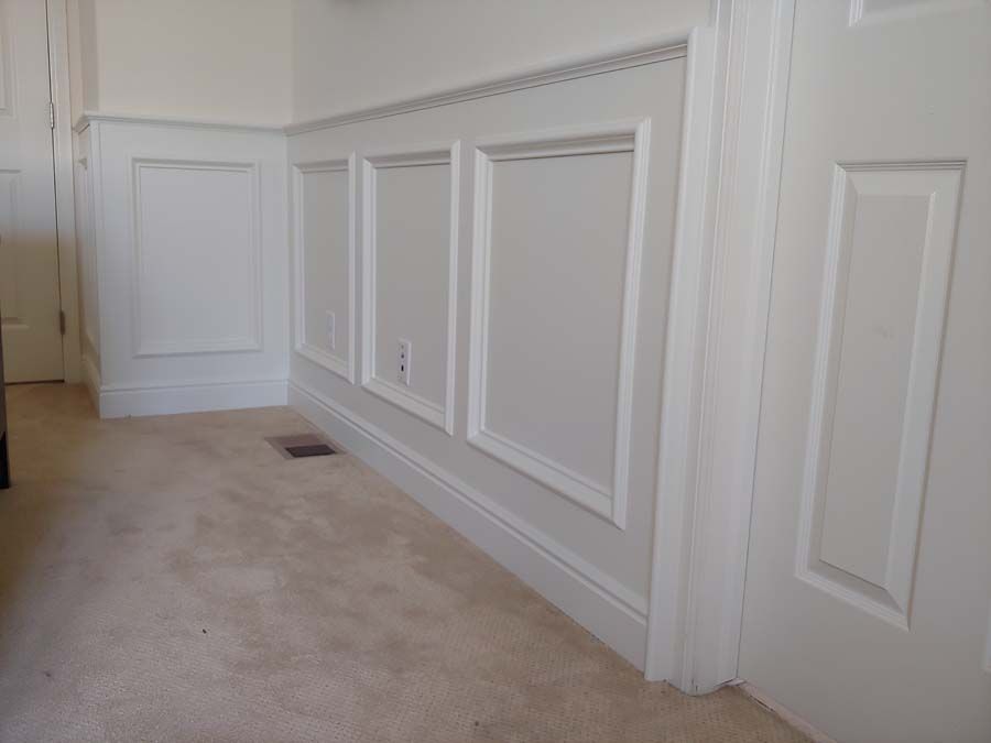 White paneled wall with decorative molding and tan carpeted floor.
