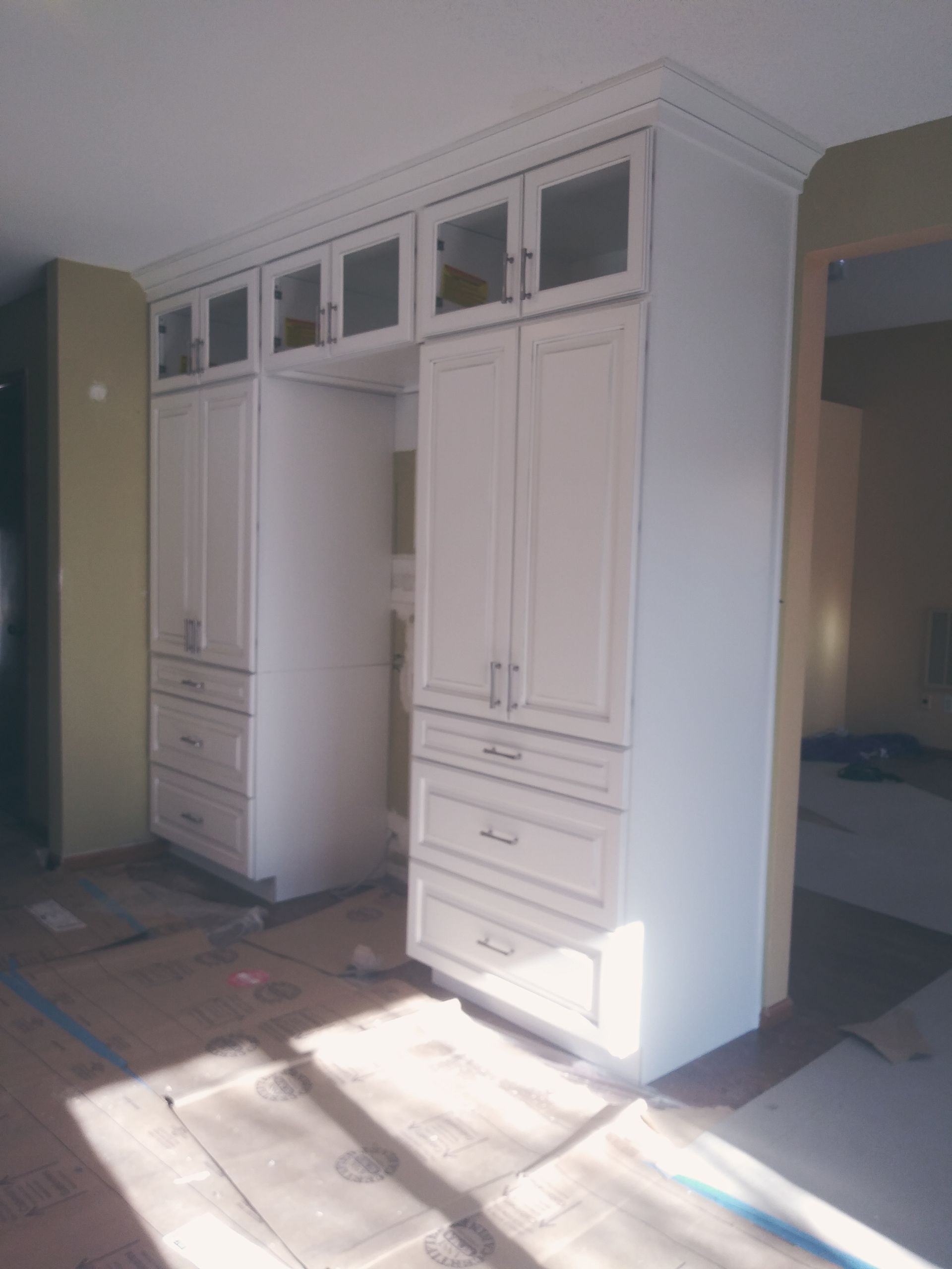 White kitchen cabinets with glass-door uppers. A refrigerator space is framed between them.