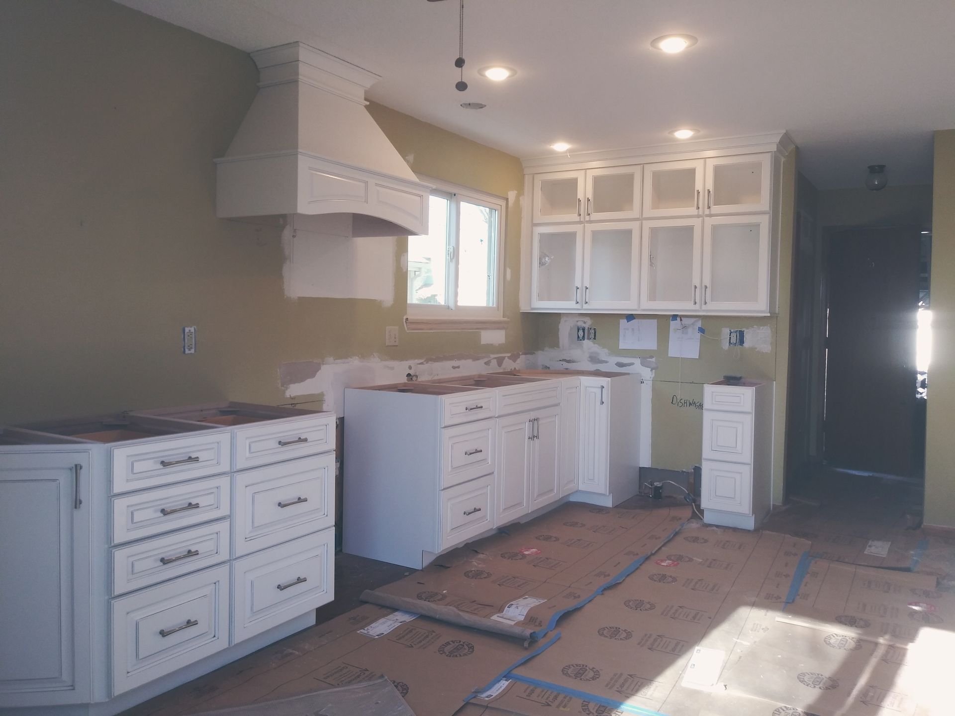 Kitchen with white cabinets, range hood, and cardboard floor covering during construction.