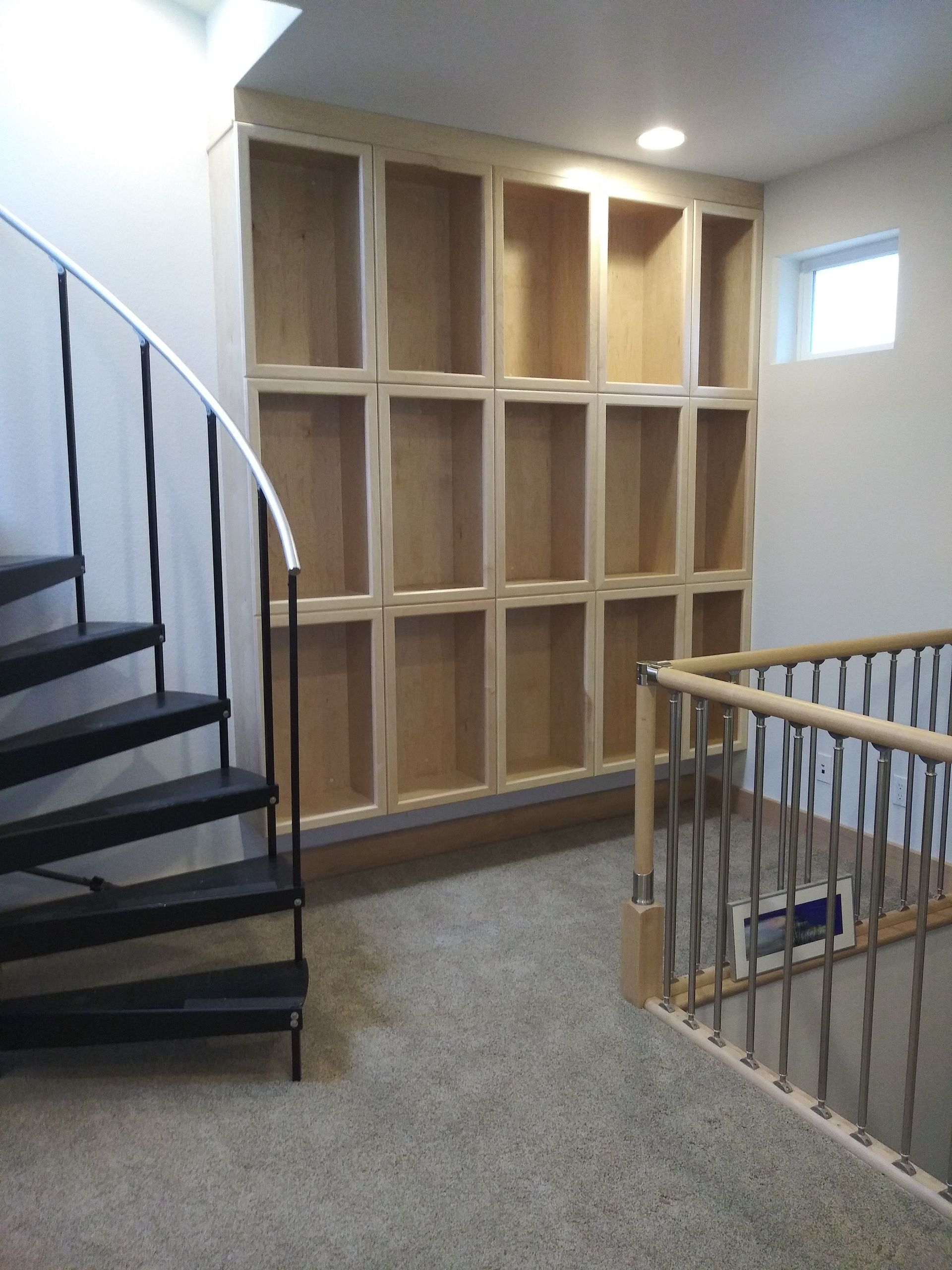 Built-in wooden shelves on a wall, with a spiral staircase on the left and a railing on the right.