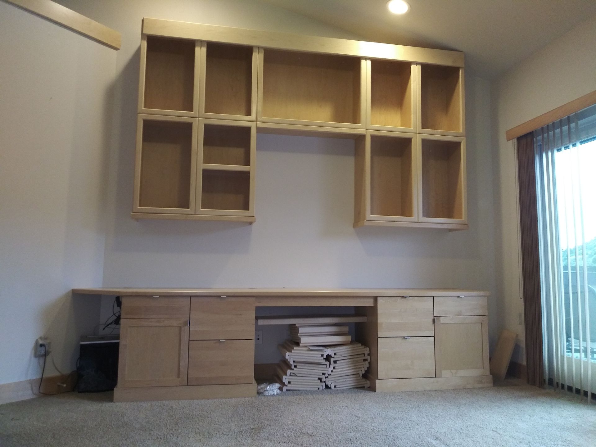 Built-in light wood cabinetry and desk against a white wall in a room with a window.