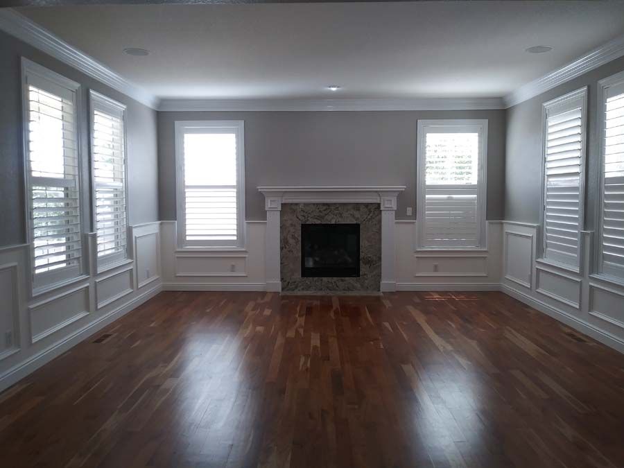 Empty room with fireplace, windows, and hardwood floors.