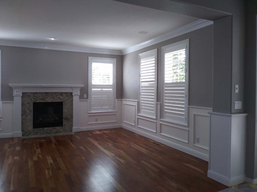 Living room with hardwood floors, fireplace, and white shutters. Gray walls, white trim.