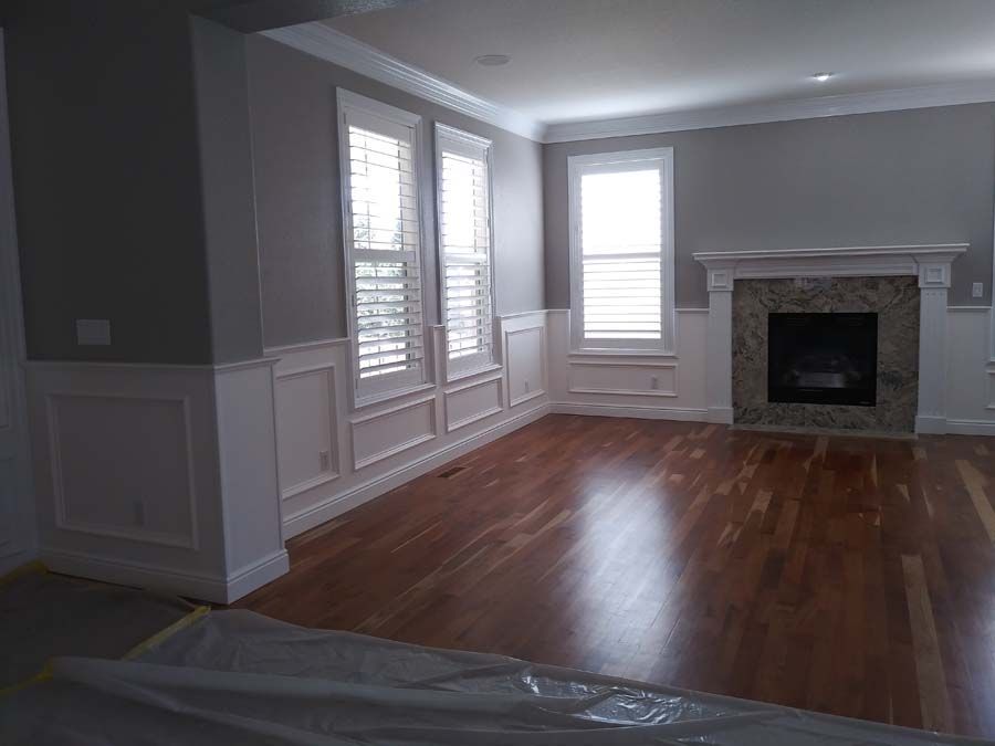Living room with hardwood floors, white trim, gray walls, and a fireplace. Windows with shutters are present.