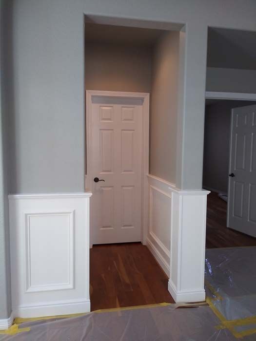 A doorway with white paneled walls and a closed white door in a room with gray walls and wood flooring.