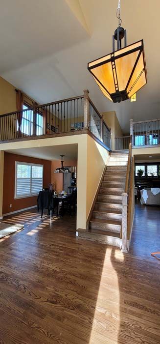 Interior view of a house with a staircase, loft, and dining area. Wooden floors and warm-toned walls.