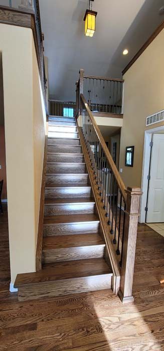 Wooden staircase in a home with hardwood flooring and a second-floor landing visible in the background.