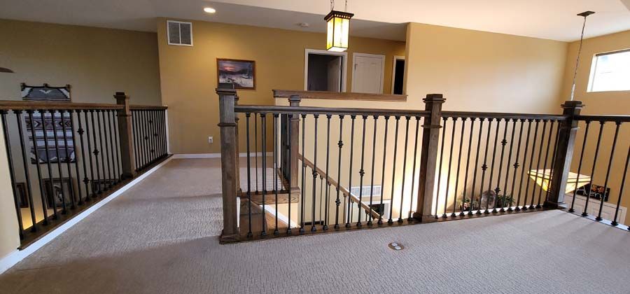 Interior view of a loft with a railing, stairs, and a hanging light fixture. Beige walls and carpet.