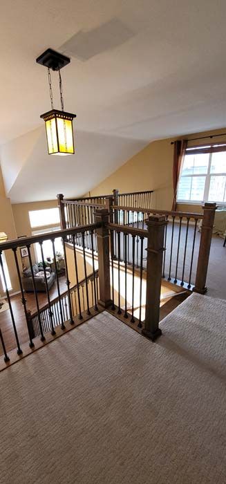 Loft with a carpeted floor, wooden railing, and a hanging light fixture. Window on the right.
