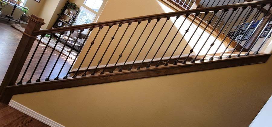 Wooden staircase with dark metal balusters, against tan walls.