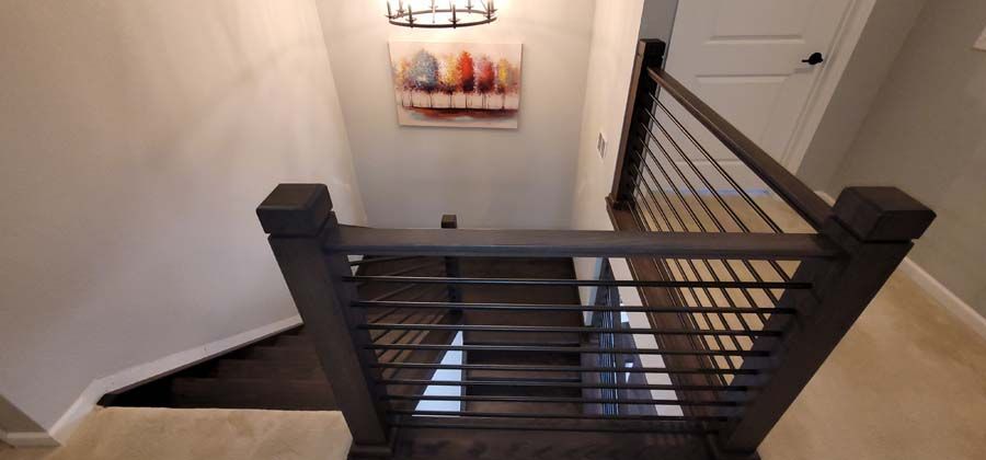 Staircase with dark wood railing and horizontal metal bars. A painting hangs on the wall, lit by a fixture.