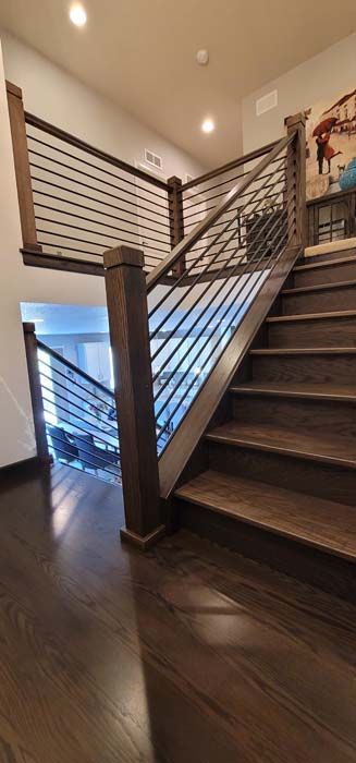 Wooden staircase with dark brown stairs and railings with black horizontal bars.