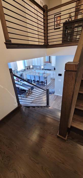 View from a staircase looking down into a kitchen. Wooden stairs and railing with horizontal metal bars.