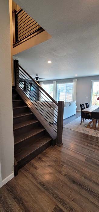 Interior view of a staircase and a living room. Dark wood stairs, a modern black railing, and wood flooring.