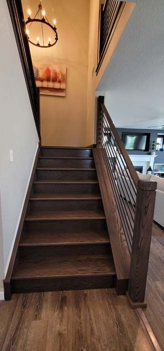 Wooden staircase with dark brown treads and railings, leading upwards. A painting and chandelier are seen.