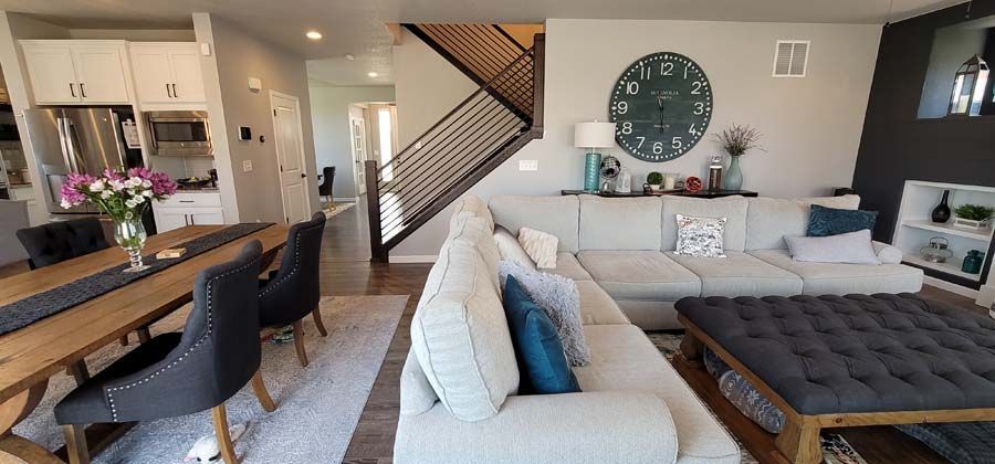 A light-filled open-plan living and dining room with a large sofa, dining table, and staircase.