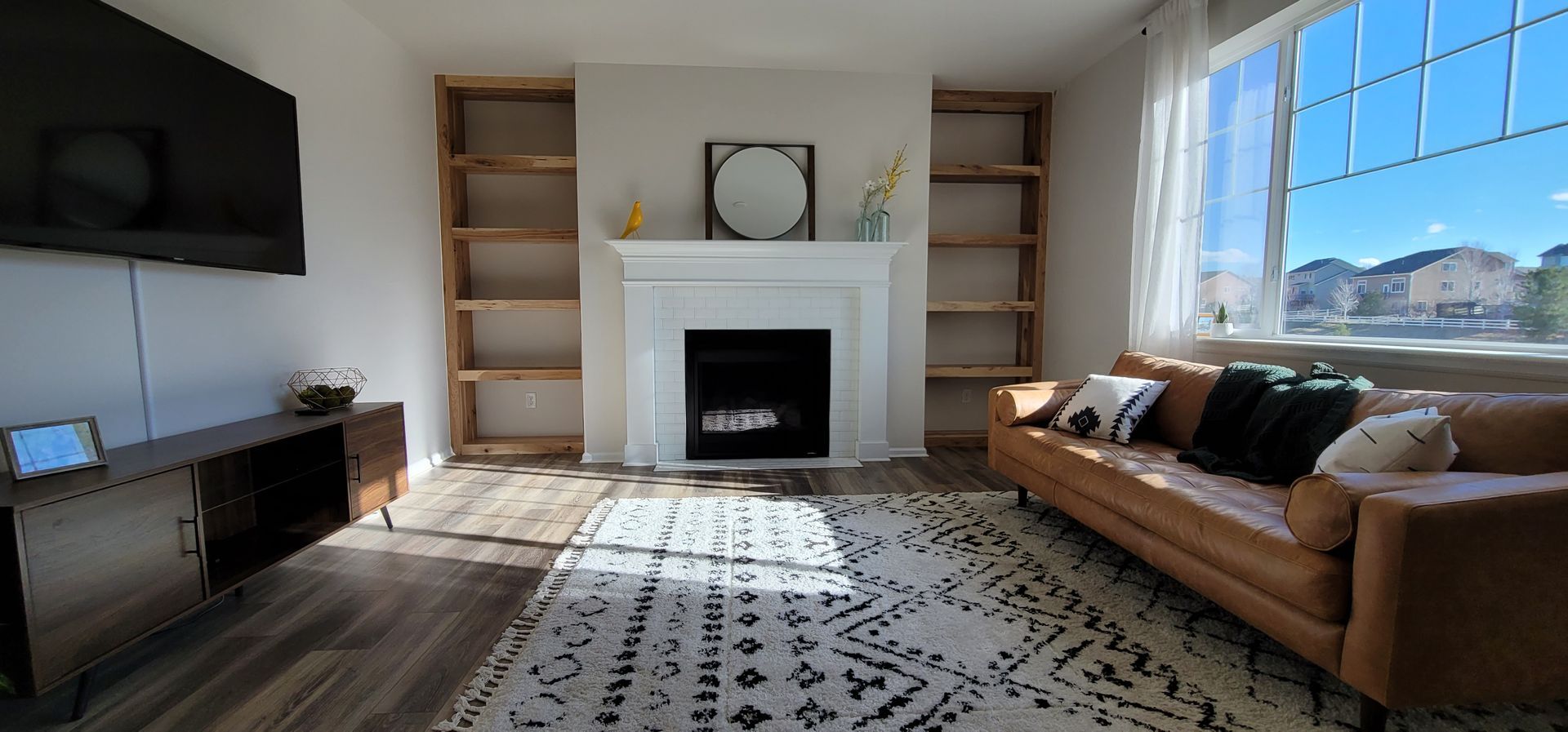 Living room with fireplace, built-in shelves, a brown leather sofa, and a large window.