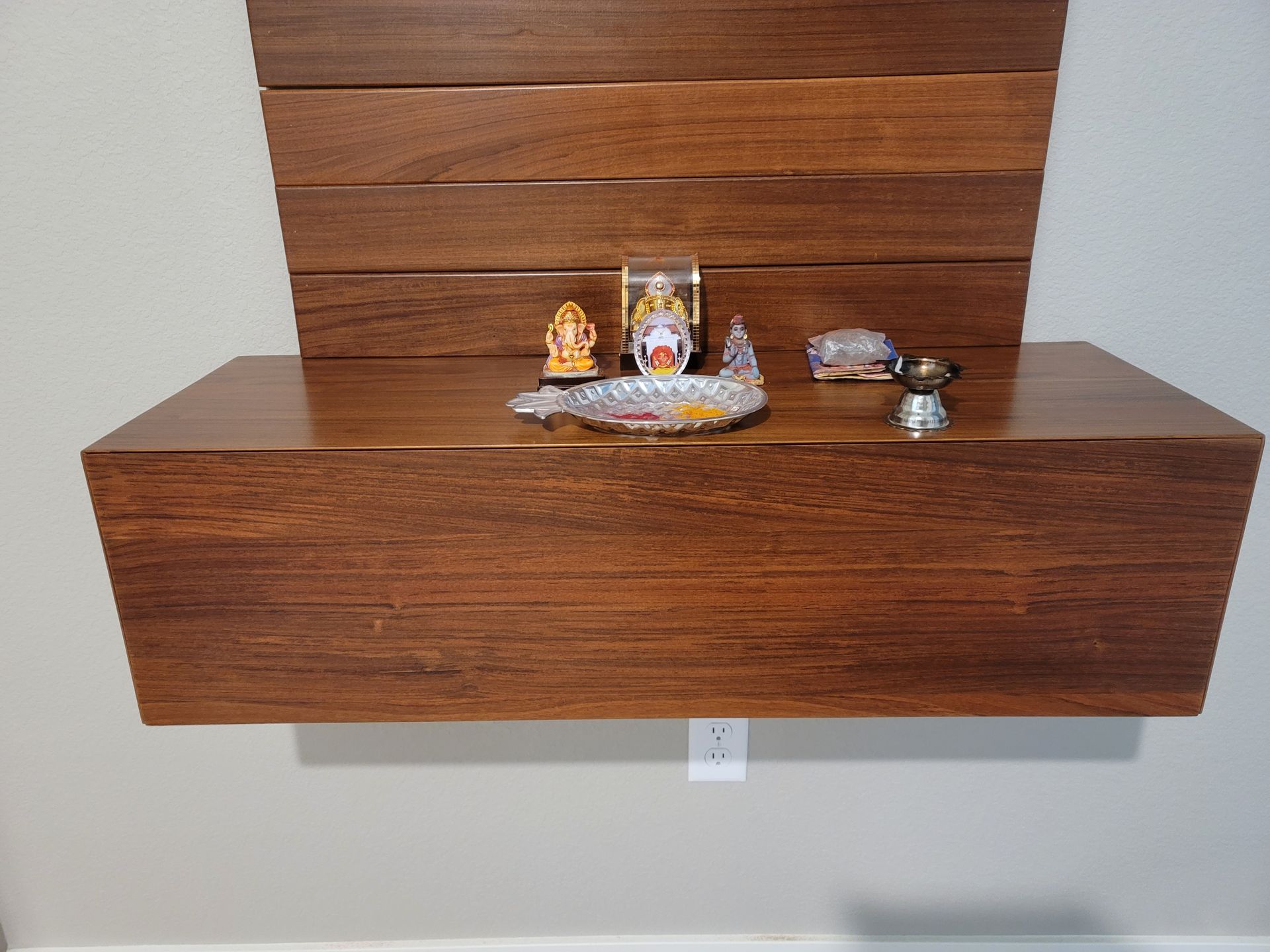 Wooden shelf with religious items on a light grey wall.