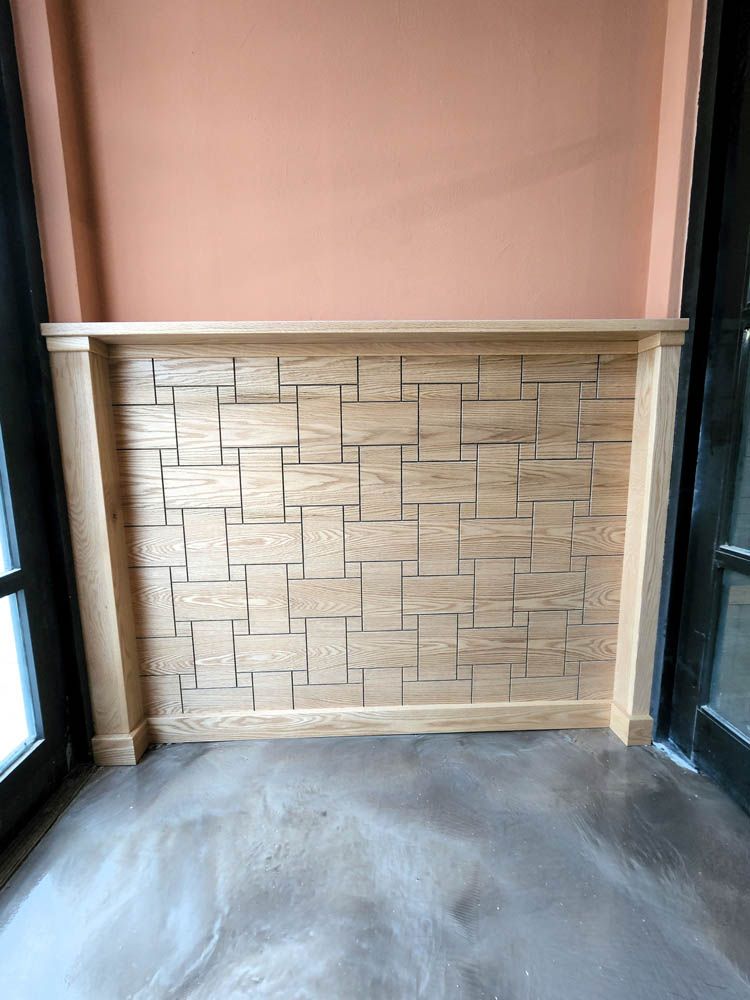 Wall with light-colored, square-patterned wooden panels, bordered by trim, against a peach-colored wall and dark doorway.