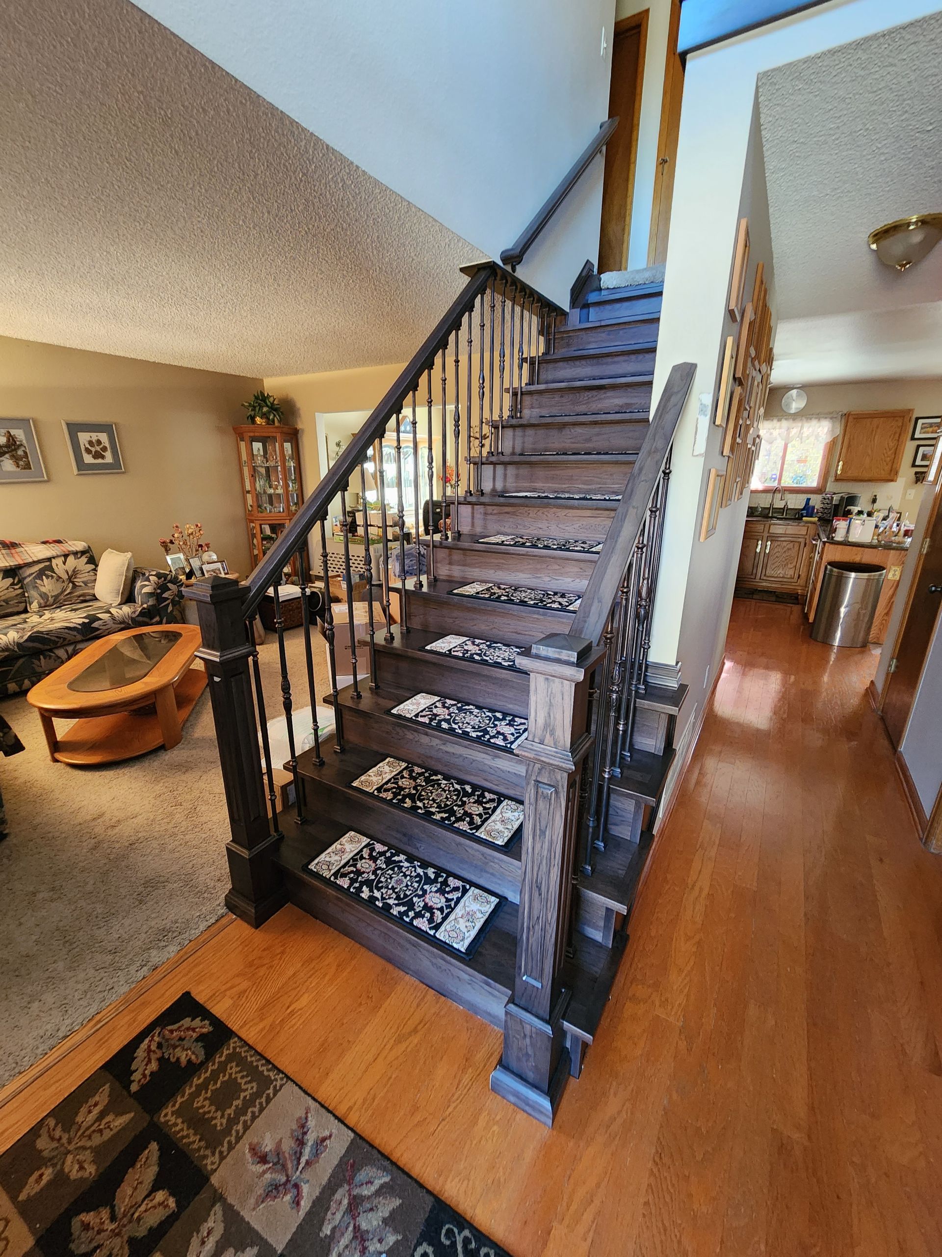 Wooden staircase with dark banister and patterned carpet runner leading to an upper level.