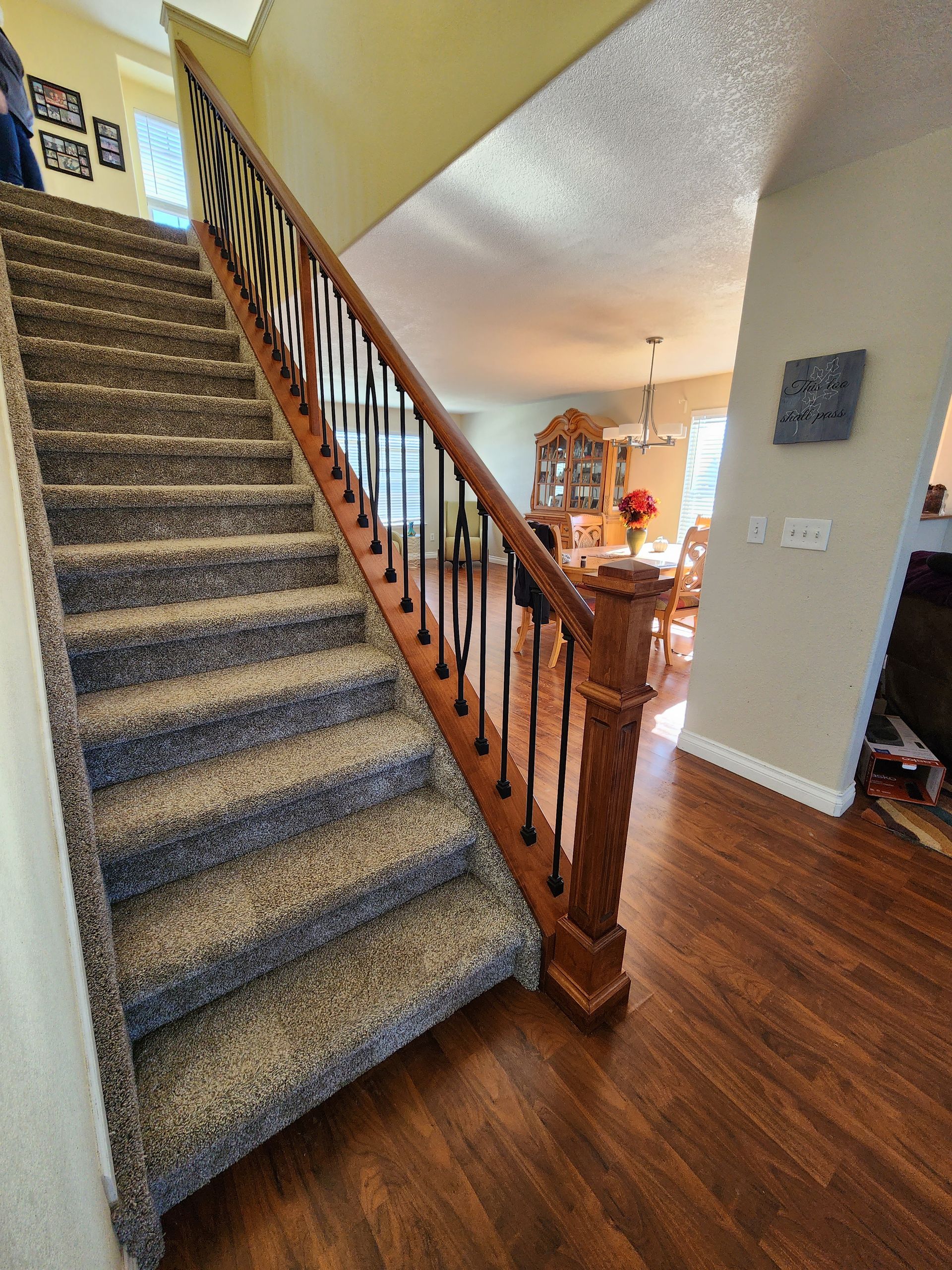Carpeted staircase with wood banister and dark metal spindles, leading up to a landing.