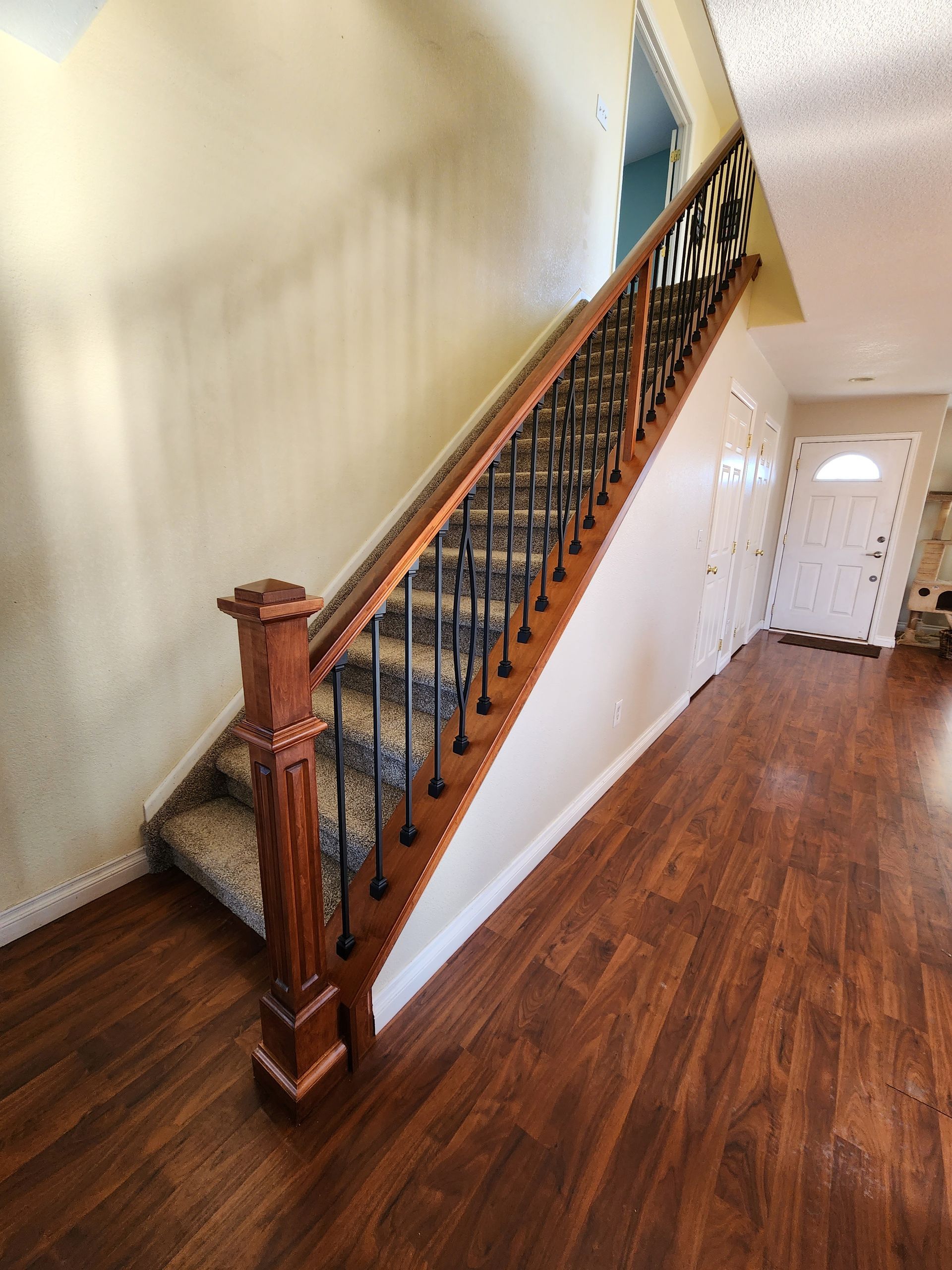 Wooden staircase with ornate black railing, beige walls, and wood floor.