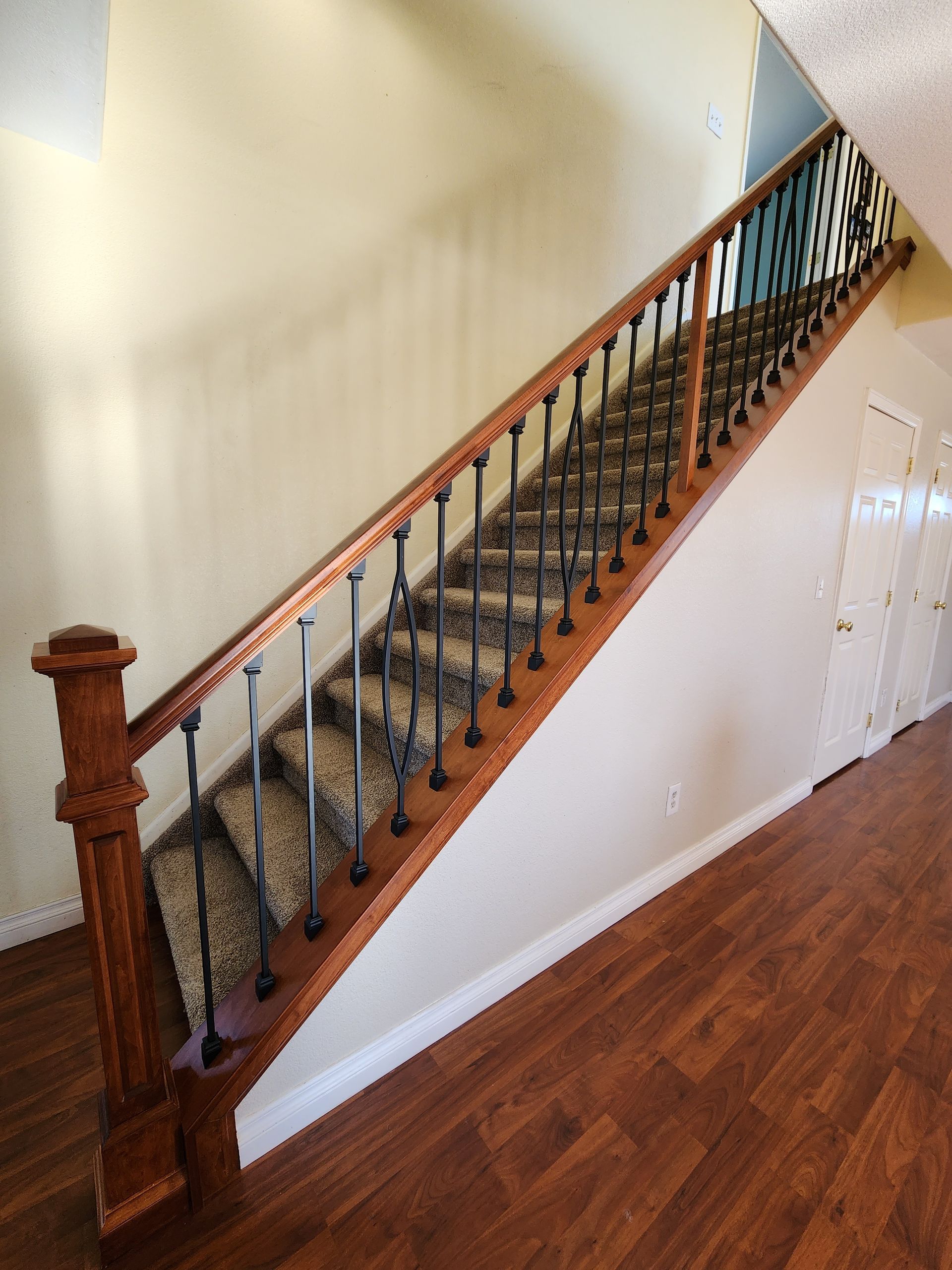 Wooden staircase with brown treads, black spindles, and a carpet runner, leading upwards.